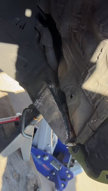 A close-up of a truck frame closed off with steel plate and a fresh weld bead, a floor jack and jack stand below.